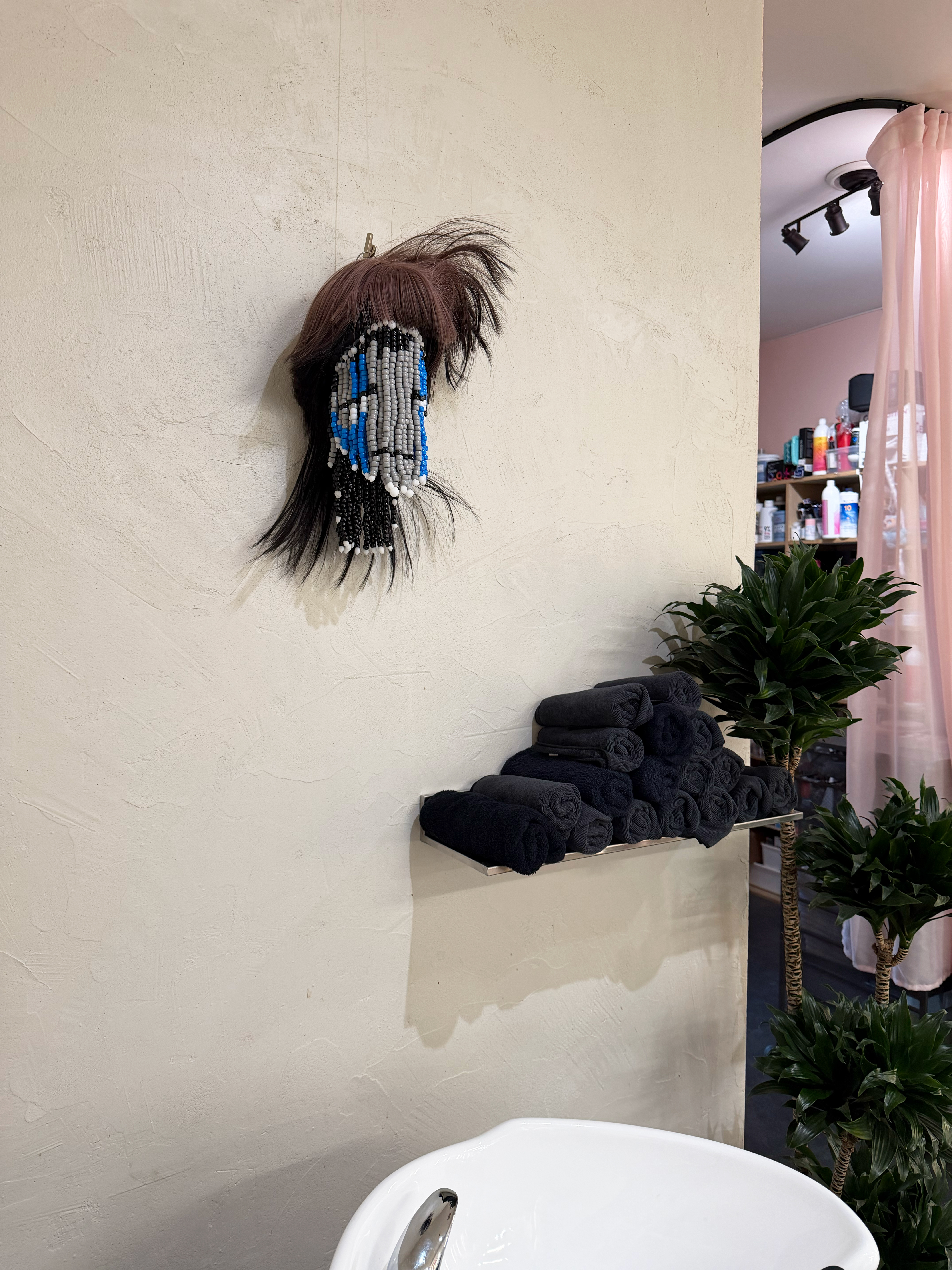Installation shot of a sculpture made using beads and a sythetic wig to represent a floating head in a salon over a washing station.